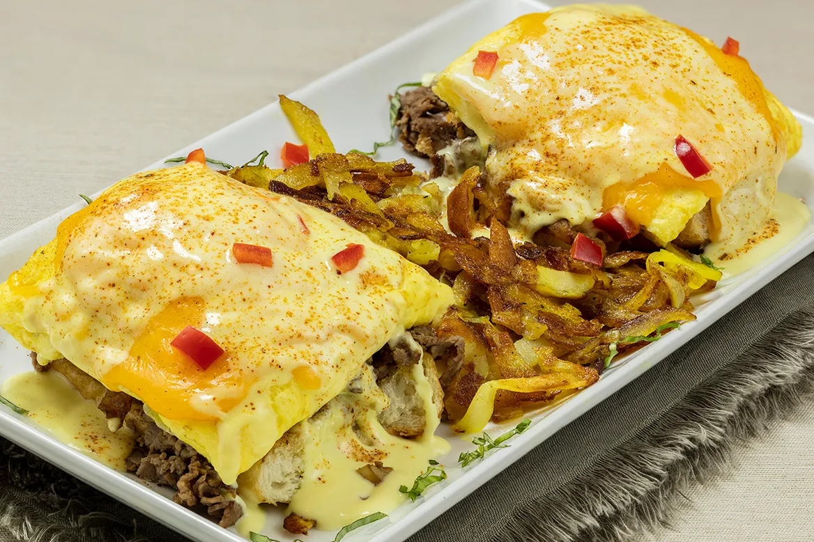 Cajun Prime Rib Benedict — scrambled eggs and cheddar cheese over seasoned prime rib on a grilled hoagie with Cajun hollandaise